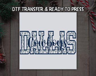 Peut inclure: Carré blanc avec le mot "DALLAS" en grandes lettres majuscules avec un motif léopard gris. Le mot "Cowboys" est écrit en cursive au centre du mot "DALLAS". Le texte "DTF TRANSFER & READY TO PRESS" est en haut.