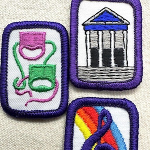 May include: Three embroidered patches with purple borders. One features a pink and green abstract design, another a building with columns, and the third a rainbow and a treble clef. All are on white fabric.