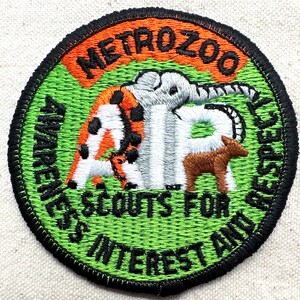 May include: Embroidered patch with the text "METROZOO" in orange, featuring an elephant, a giraffe, and a brown animal. The patch has a green background with additional text and a black border.
