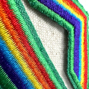 Puede incluir: Primer plano de dos parches bordados con un dise&ntilde;o de arco&iacute;ris. Los parches presentan colores vibrantes que incluyen rojo, naranja, amarillo, verde, azul y morado. Los bordes est&aacute;n delineados con hilo verde.