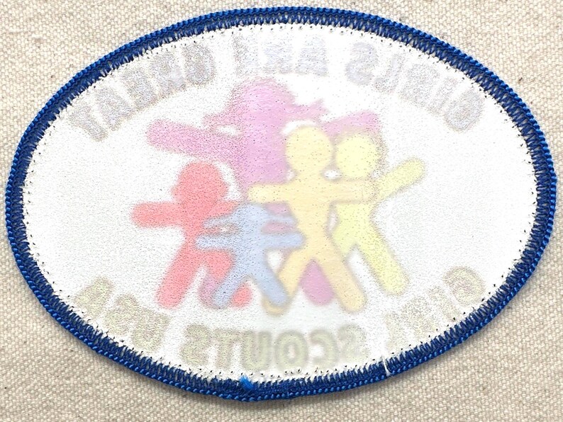May include: Oval patch with a blue border and white background. The patch features colourful stick figures in red, purple, blue, and yellow. The text "GIRLS AND GREAT SCOUTS" is visible.