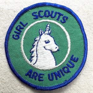 May include: Embroidered patch with a green background and a blue border. The patch features a white unicorn inside a white circle. The text "GIRL SCOUTS ARE UNIQUE" is embroidered in blue around the unicorn.