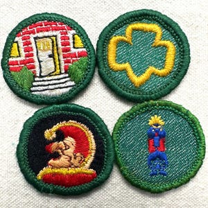 May include: Four embroidered patches with green borders. Designs include a house, a yellow trefoil, a jester, and a figure in blue and red. The patches are circular and have a textured appearance.