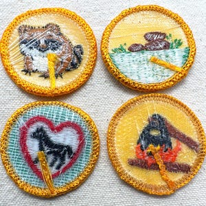 May include: Four round embroidered patches with yellow borders. One features a raccoon, another a bowl with rocks, a third a horse in a heart, and the last a bird on a branch. Each has a yellow thread.