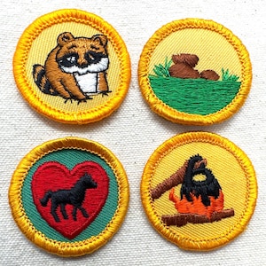 May include: Four embroidered patches with yellow borders. One features a raccoon, another a bear in grass, a third a black horse in a red heart, and the last a campfire. These patches are likely for a youth organization.