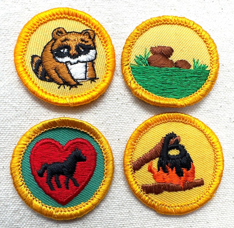 May include: Four embroidered patches with yellow borders. One features a raccoon, another a bear in grass, a third a black horse in a red heart, and the last a campfire. These patches are likely for a youth organization.