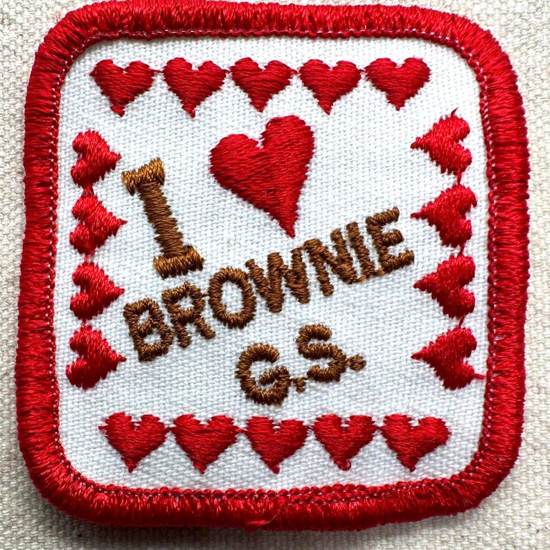 May include: Square embroidered patch with a white background, red border, and red heart accents. The patch features the text "I BROWNIE G.S." in brown thread, with a large red heart in the center.