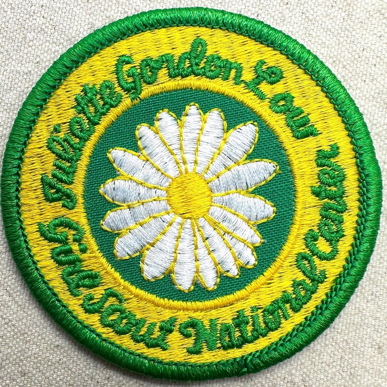 Puede incluir: Parche bordado con borde verde y centro amarillo y verde. El centro presenta una margarita blanca con centro amarillo. El texto bordado en amarillo dice "Juliette Gordon Low" y "Girl Scout National Center".
