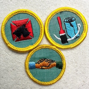 May include: Three embroidered patches with a green background and yellow border. One patch features a red and black design, another shows a paintbrush and rolled-up blue fabric, and the third depicts a handshake.