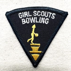 Puede incluir: Parche triangular negro con texto bordado blanco "GIRL SCOUTS BOWLING". Una figura amarilla de un jugador de bolos est&aacute; sobre un pedestal amarillo. El parche tiene un borde negro.