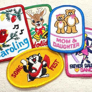 May include: A collection of embroidered patches with various designs. One patch features a red cardinal singing with the word "Caroling". Other patches include a reindeer, teddy bears with "Mom & Daughter", a cat with "Song Fest", and a couple dancing with "Father Daughter Dance".
