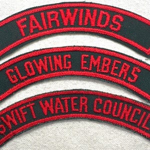 May include: Three embroidered patches with arched shapes. Each patch has a black background with red text and a red border. The top patch reads "FAIRWINDS", the middle patch reads "GLOWING EMBERS", and the bottom patch reads "SWIFT WATER COUNCIL".