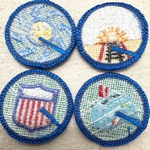 May include: Four round embroidered patches with blue borders. Each patch features a different design: a sun, a shield with red and white stripes, a stylized design, and a design with a blue and white object.
