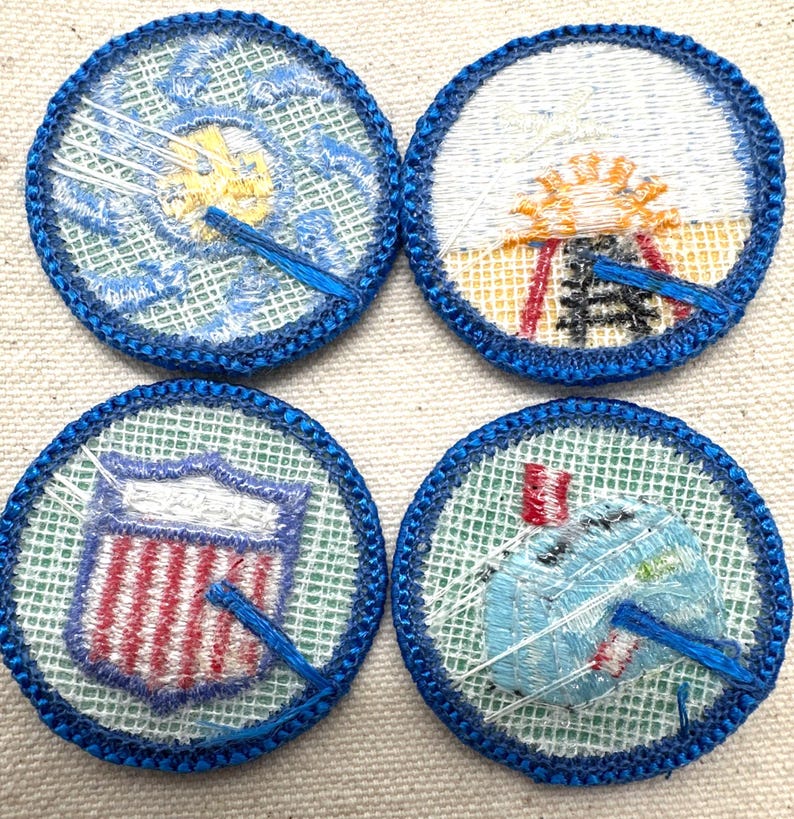 May include: Four round embroidered patches with blue borders. Each patch features a different design: a sun, a shield with red and white stripes, a stylized design, and a design with a blue and white object.