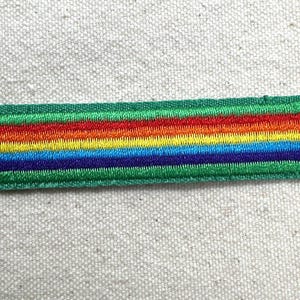 Puede incluir: Parche bordado con dise&ntilde;o de arco&iacute;ris, con rayas rojas, naranjas, amarillas, verdes, azules y moradas. El parche tiene un borde verde y forma rectangular. Para ropa o accesorios.