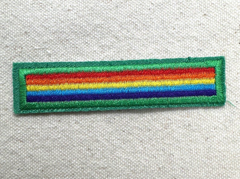 Puede incluir: Parche bordado con dise&ntilde;o de arco&iacute;ris, con rayas rojas, naranjas, amarillas, verdes, azules y moradas. El parche tiene un borde verde y forma rectangular. Para ropa o accesorios.