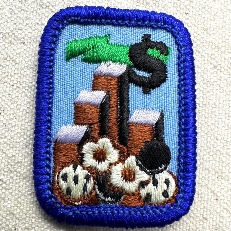 May include: Embroidered patch with a blue border and a light blue background. The design features a black dollar sign, brown structures, green leaves, white and black flowers, and a black object.