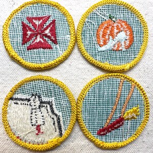May include: Four round embroidered patches with yellow borders. The patches feature designs of a red cross, an orange pumpkin, a white and black figure, and a red and yellow object. The patches are on a light green mesh background.