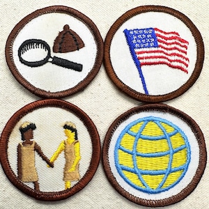 May include: Four embroidered patches with brown borders. One features a magnifying glass and a detective hat, another an American flag, a third shows two figures shaking hands, and the last depicts a globe.