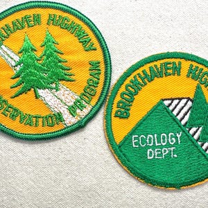 May include: Two circular embroidered patches. One features a road and green trees on a yellow background, with the text "Brookhaven Highway Conservation Program." The other patch has a green triangle with trees and the text "Ecology Dept."