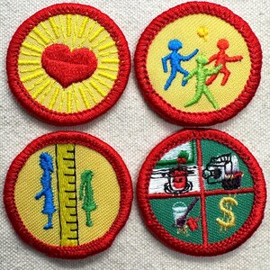 May include: Four circular embroidered patches with red borders. One features a red heart on a yellow sunburst. Another shows blue, green, and red figures on yellow. A third depicts blue and green silhouettes by a ruler. The fourth has four quadrants.