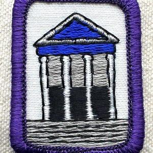 May include: Embroidered patch featuring a building with a blue roof and columns. The patch has a white background and a purple border. The building's columns are black, white, and gray. The patch is rectangular.