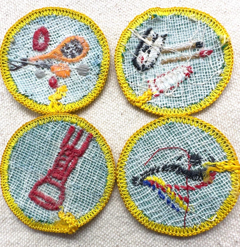 May include: Four round embroidered patches with yellow stitched borders. Each patch features a different design: a lacrosse stick, a rocket, a red tool, and a bow and arrow. The patches have a light blue background.
