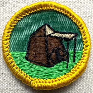 Pu&ograve; includere: Toppa ricamata rotonda raffigurante una tenda marrone con tetto beige, su sfondo verde. La toppa ha un bordo cucito giallo. Ideale per gli appassionati di campeggio o attivit&agrave; all'aperto.
