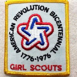 May include: Square patch with a white background, featuring a red, white, and blue star design. The patch is embroidered with the words "AMERICAN REVOLUTION BICENTENNIAL" and "GIRL SCOUTS" in black and red, with the years "1776-1976". The patch has a yellow border.