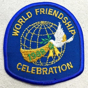K&ouml;nnte beinhalten: Blauer, gestickter Aufn&auml;her mit den Worten "WORLD FRIENDSHIP CELEBRATION" und "1998". Der Aufn&auml;her zeigt einen goldenen Globus, eine wei&szlig;e Taube und ein Banner mit gr&uuml;nen Bl&auml;ttern.