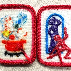 Puede incluir: Dos parches bordados con bordes rojos. Uno presenta una olla roja con flores y una base negra. El otro muestra una figura azul en un arco y una figura roja. Ambos parches tienen un fondo blanco.