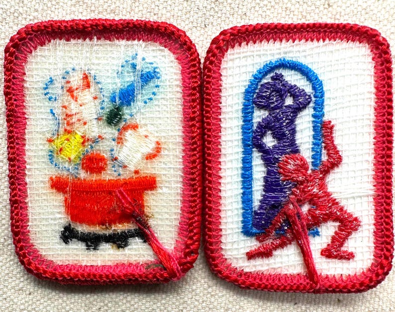 Puede incluir: Dos parches bordados con bordes rojos. Uno presenta una olla roja con flores y una base negra. El otro muestra una figura azul en un arco y una figura roja. Ambos parches tienen un fondo blanco.