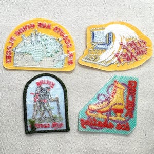 May include: Four embroidered patches with various designs. One yellow patch features a building and text. Another yellow patch shows a computer and a wave. A green and white patch depicts hikers. A teal patch displays a roller skate.