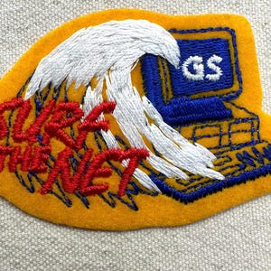 May include: Embroidered patch with a yellow background, featuring a white wave and a blue computer. The text "SURF THE NET" is in red. The computer screen displays "GS".