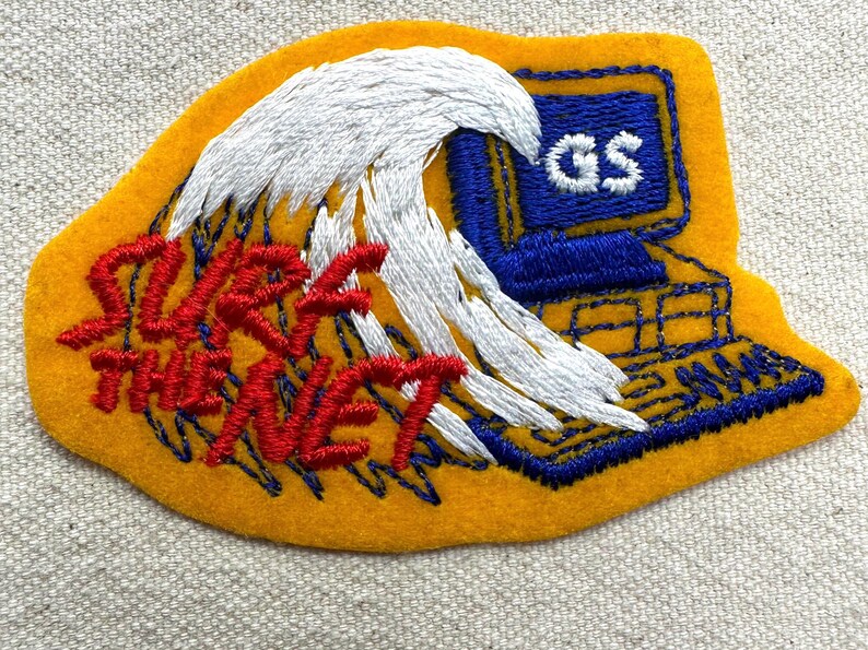 May include: Embroidered patch with a yellow background, featuring a white wave and a blue computer. The text "SURF THE NET" is in red. The computer screen displays "GS".