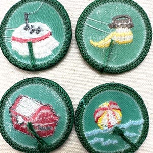 May include: Four round green embroidered patches with various designs. One patch features a white and red umbrella, another a yellow and brown object, a red structure, and a beach ball in water. Each patch has a green border.
