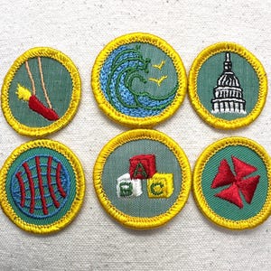 May include: Six embroidered patches with yellow borders and green backgrounds. Designs include a swing, a wave with birds, the U.S. Capitol building, a globe, alphabet blocks, and a red pinwheel. The patches are circular.