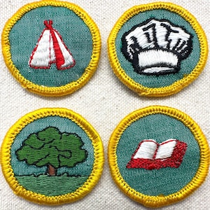 May include: Four embroidered patches with yellow borders and teal backgrounds. The patches feature a white and red tent, a chef's hat, a green tree, and an open book with red covers. These patches are likely for a youth organization.