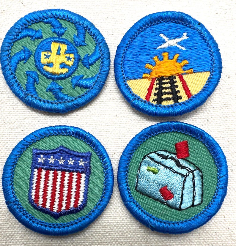 May include: Four embroidered patches with blue borders. The patches feature various designs, including a recycling symbol, a train with a sun and airplane, a shield with stars and stripes, and a building with a red chimney. The patches are on a green background.