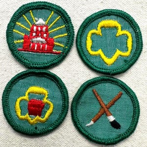 May include: Four circular green patches with embroidered designs. One features a red building with yellow rays, another a yellow trefoil, a third a red and yellow design, and the last crossed paintbrushes.
