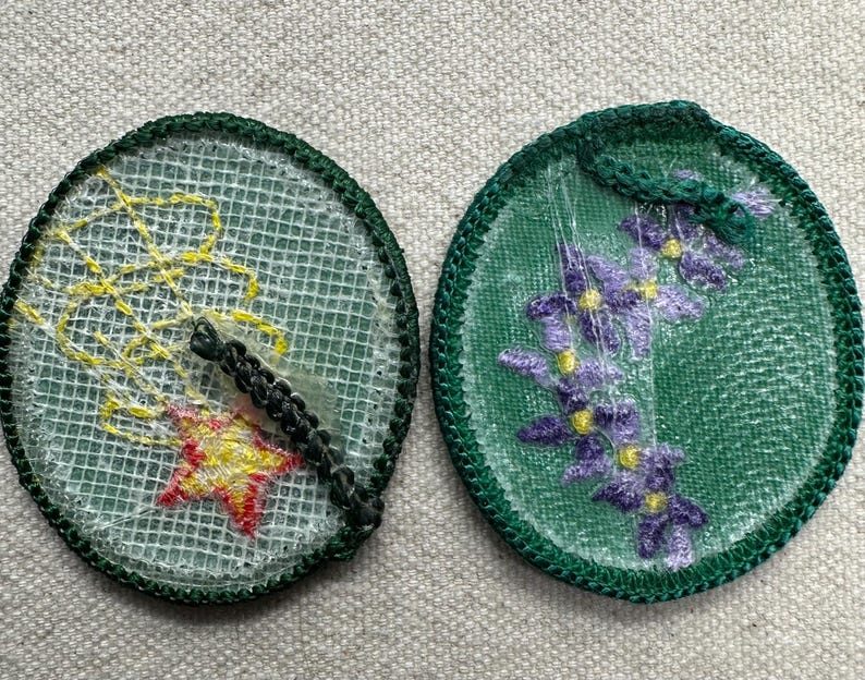 May include: Two round embroidered patches. One features a yellow and red star with yellow lines on a white mesh background, and a black border. The other has purple flowers on a green mesh background with a green border.