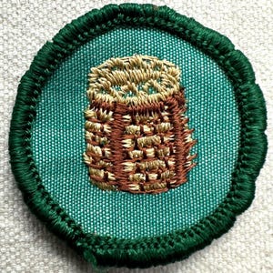 May include: A round, embroidered patch featuring a detailed owl design. The owl is rendered in shades of brown and tan, with a textured appearance. The patch has a teal background and a dark green, stitched border.