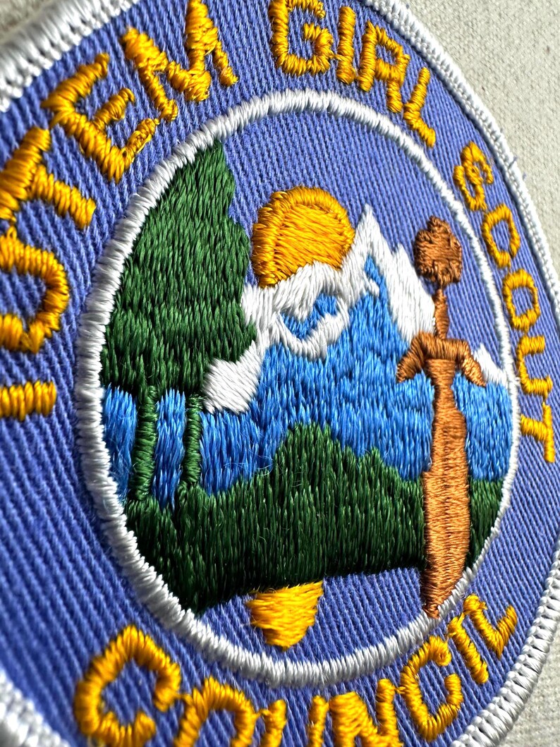 K&ouml;nnte beinhalten: Gestickter Aufn&auml;her mit dem Text "STEM GIRL SCOUT COUNCIL" in goldener Schrift auf blauem Grund. Der Aufn&auml;her zeigt eine Berglandschaft mit gelber Sonne, gr&uuml;nen B&auml;umen und blauen Bergen.