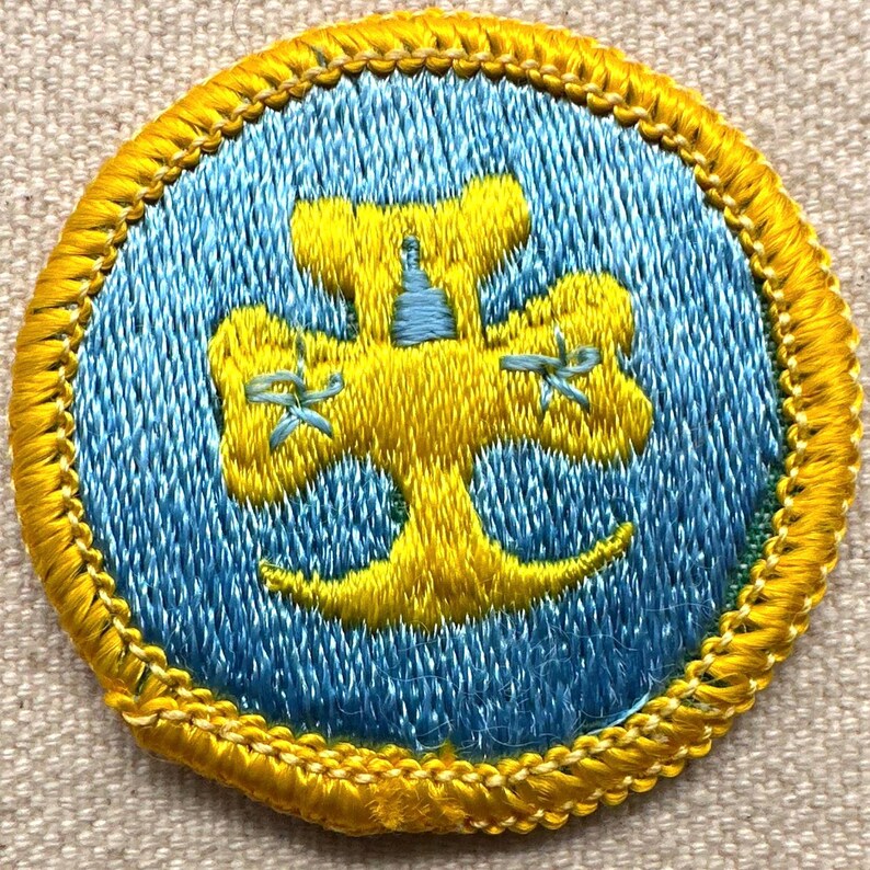 May include: Embroidered patch with a yellow and blue design. The circular patch features a yellow emblem on a blue background, surrounded by a yellow border. The emblem appears to be a stylized tree or floral design.