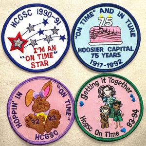 May include: Four embroidered patches with various designs and text. One patch features a star design with the text "I'm an On Time Star". Another has a cake with musical notes and "75 Years". A third shows a bunny and the text "Hoppin' In". The last patch has a group of girls and the text "Getting It Together".