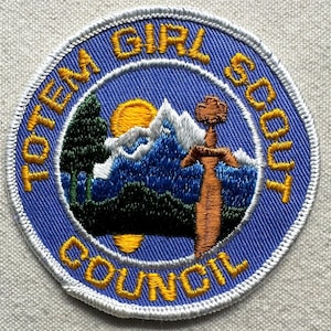 K&ouml;nnte beinhalten: Gestickter Aufn&auml;her mit den Worten "TOTEM GIRL SCOUT COUNCIL" in Gelb auf blauem Hintergrund. Der Aufn&auml;her zeigt eine Berglandschaft mit aufgehender Sonne, einem Baum und einem Schwert.