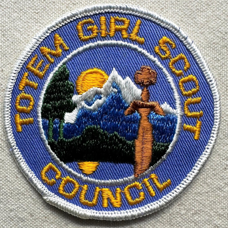 K&ouml;nnte beinhalten: Gestickter Aufn&auml;her mit den Worten "TOTEM GIRL SCOUT COUNCIL" in Gelb auf blauem Hintergrund. Der Aufn&auml;her zeigt eine Berglandschaft mit aufgehender Sonne, einem Baum und einem Schwert.