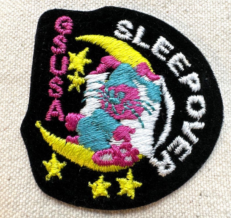 K&ouml;nnte beinhalten: Gestickter Aufn&auml;her mit schwarzem Hintergrund, mit einem gelben Halbmond, Sternen und einem skurrilen Design in Pink, Blau und Wei&szlig;. Der Aufn&auml;her tr&auml;gt die Aufschrift "SLEEPOVER" und "S.A.S.S.A."