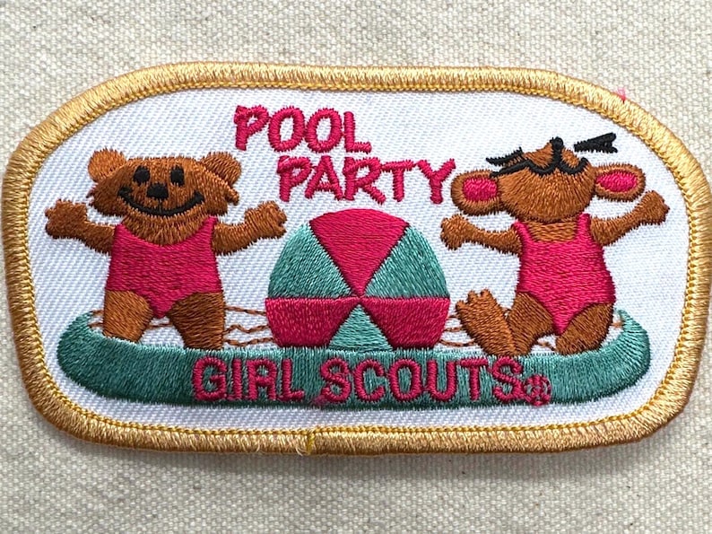May include: Embroidered patch with a white background and gold trim. The patch features two brown bear-like characters in pink swimsuits, a beach ball, and the words "POOL PARTY GIRL SCOUTS" in pink and green.