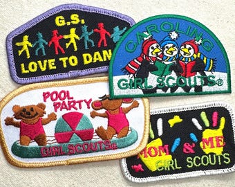 May include: A collection of Girl Scout patches with various designs. One patch features dancing figures, another shows penguins reading, and a third depicts bears at a pool party. Other patches include the phrases "Mom & Me" and "Love to Dan".